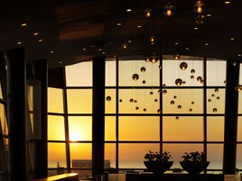 Una habitación con ventanas amplias, vista al atardecer y lámparas esféricas colgantes.