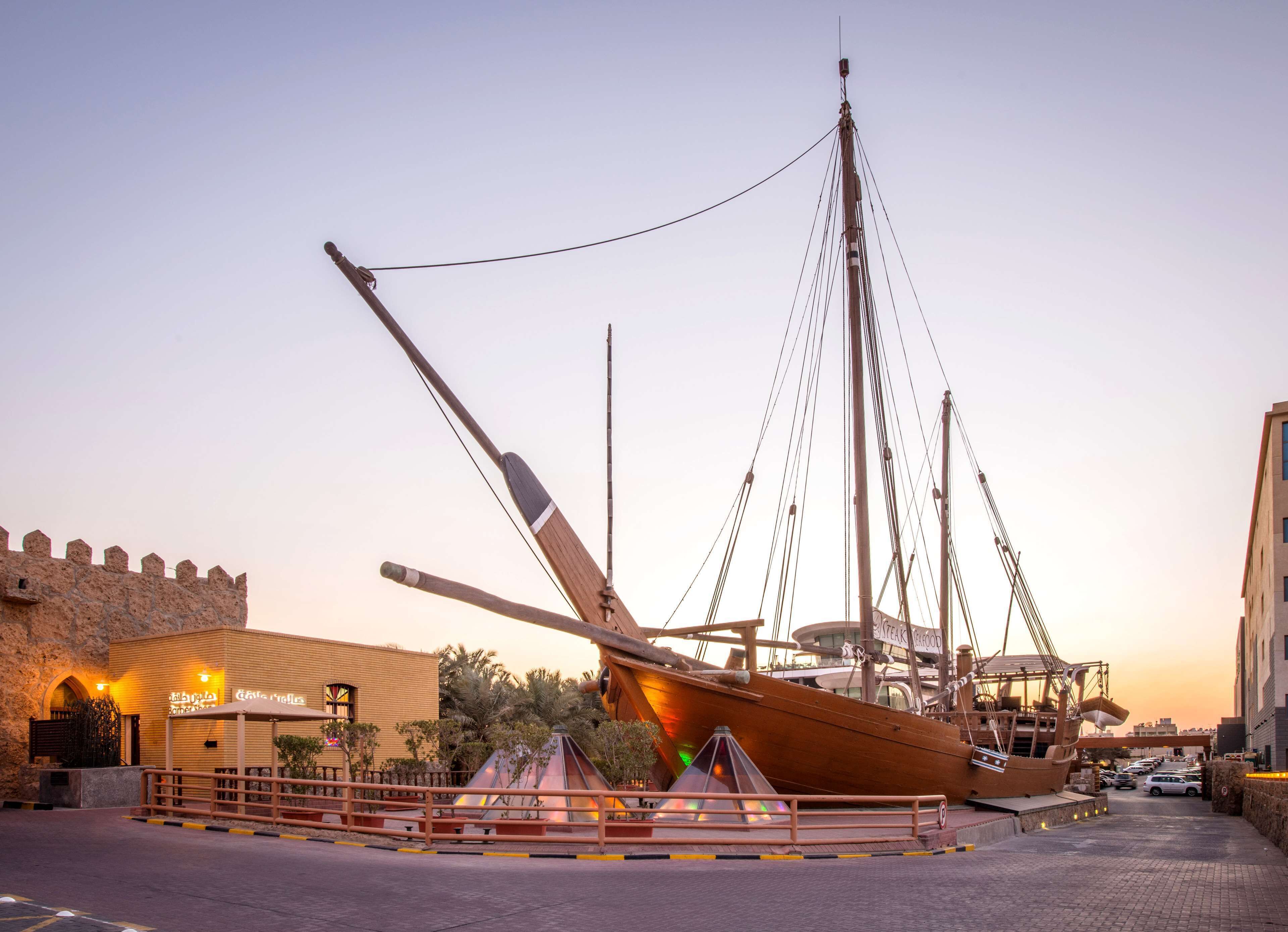 Een groot schip afgemeerd in een haven, met een stenen gebouw en een restaurant op de achtergrond.