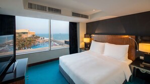 A hotel room with a large bed, a TV, a desk, and a view of a pool and buildings.