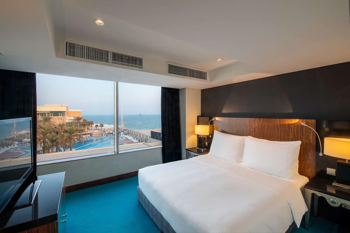 A hotel room with a large bed, a TV, a desk, and a view of a pool and buildings.