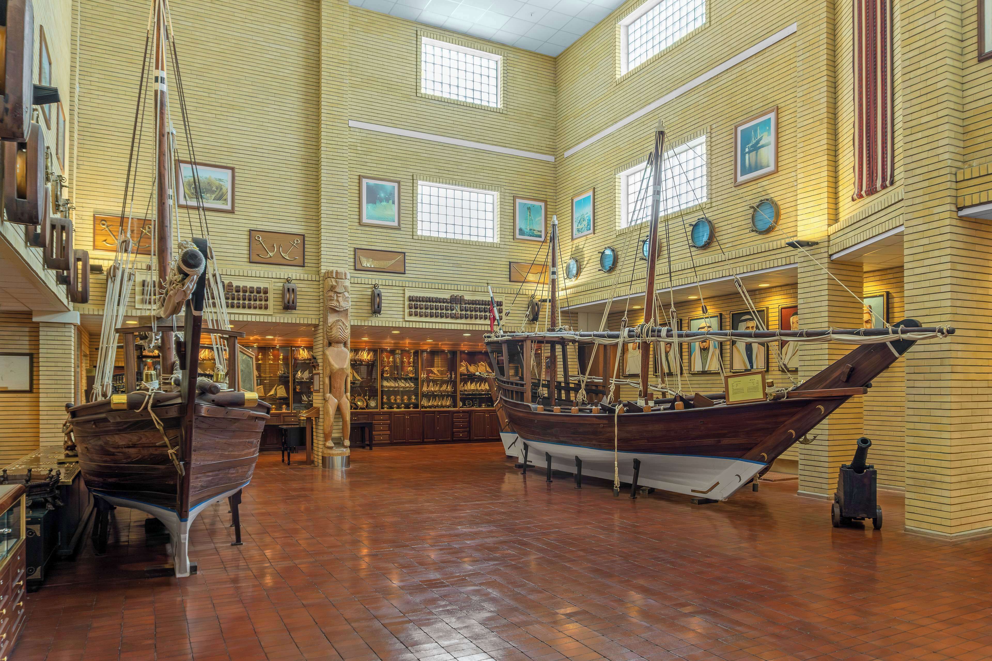 Museu amb grans vaixells de fusta exposats, un sostre alt i una paret de maó amb quadres emmarcades.