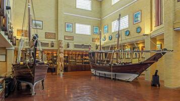 A museum with large wooden boats on display, a high ceiling, and a brick wall with framed pictures.