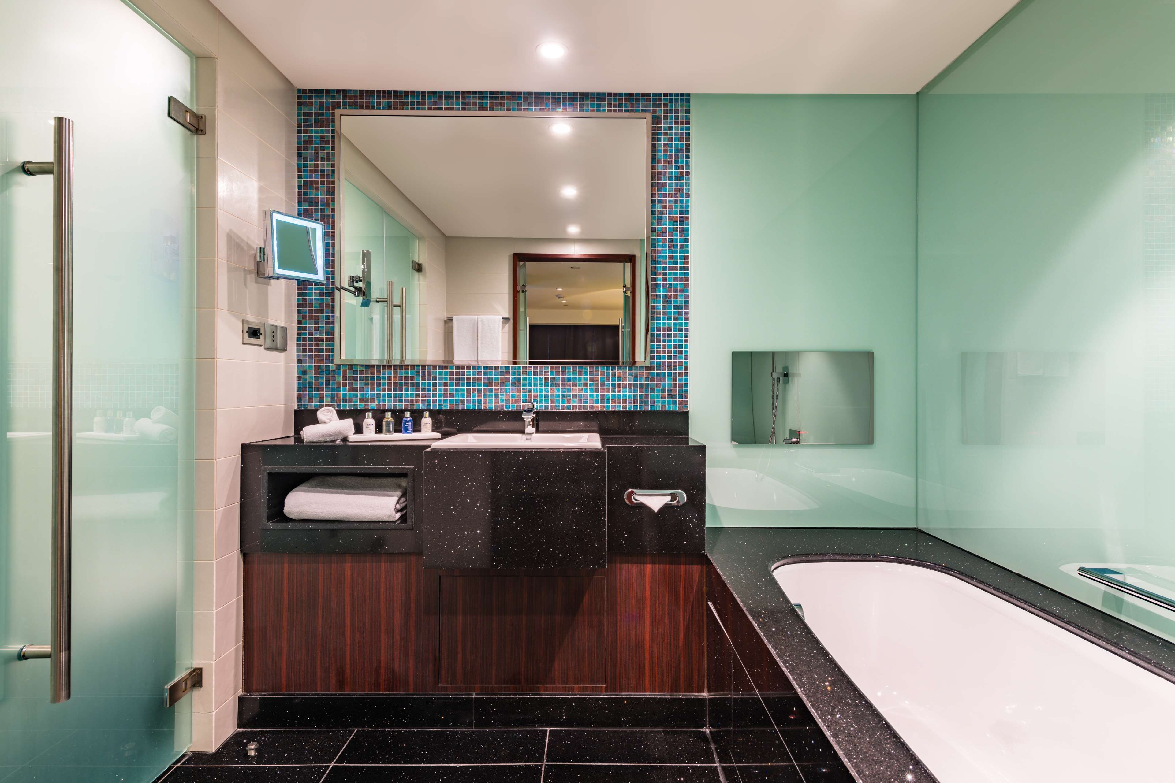 A modern bathroom with a large mirror, a bathtub, and a vanity with a sink and towel rack.