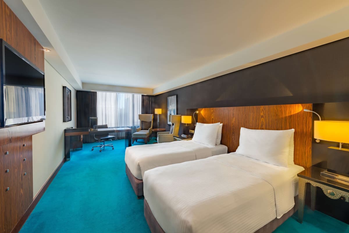 A hotel room with two beds, a desk, a chair, a TV, and a window with curtains.