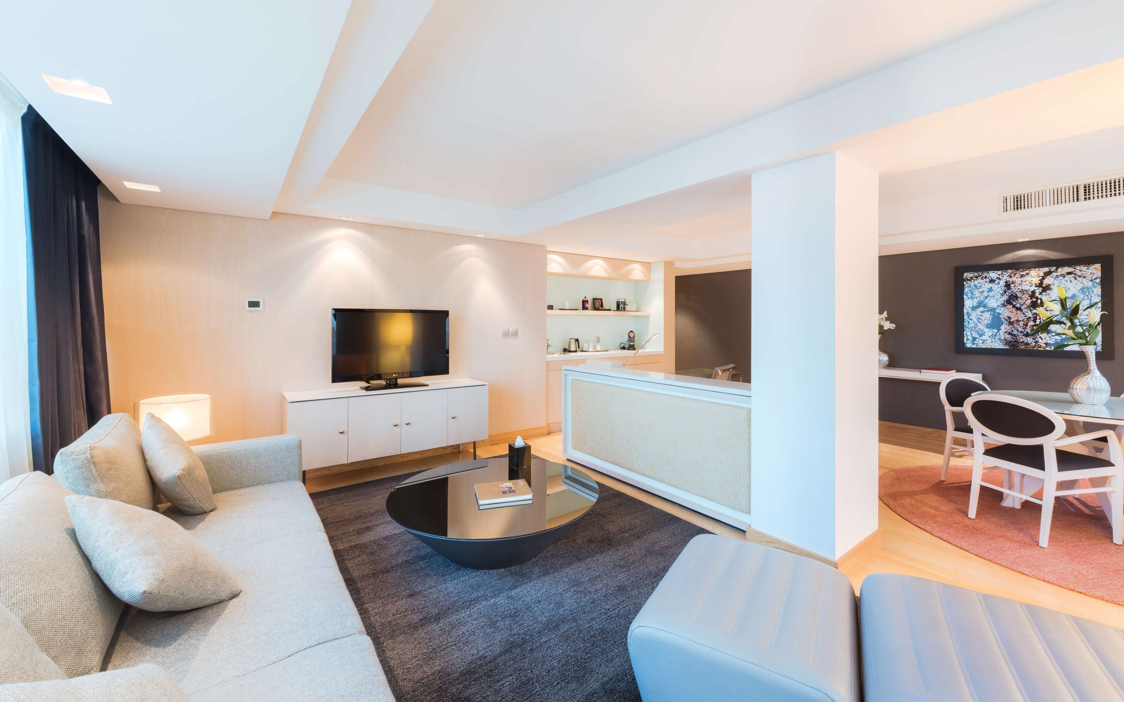 Una sala de estar moderna con un sofá, una mesa de centro, un televisor y un comedor con sillas y una mesa.