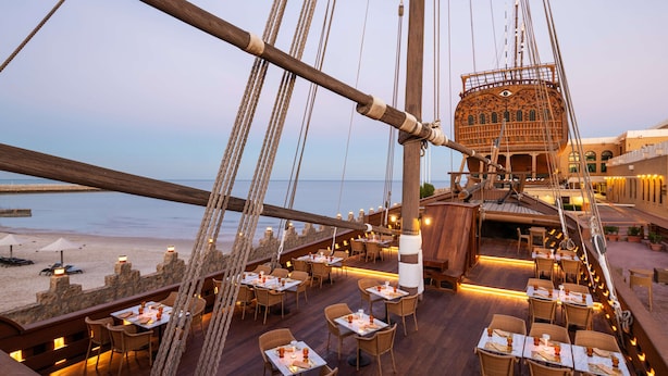 A dining area on a ship with tables and chairs arranged for guests, overlooking the sea.