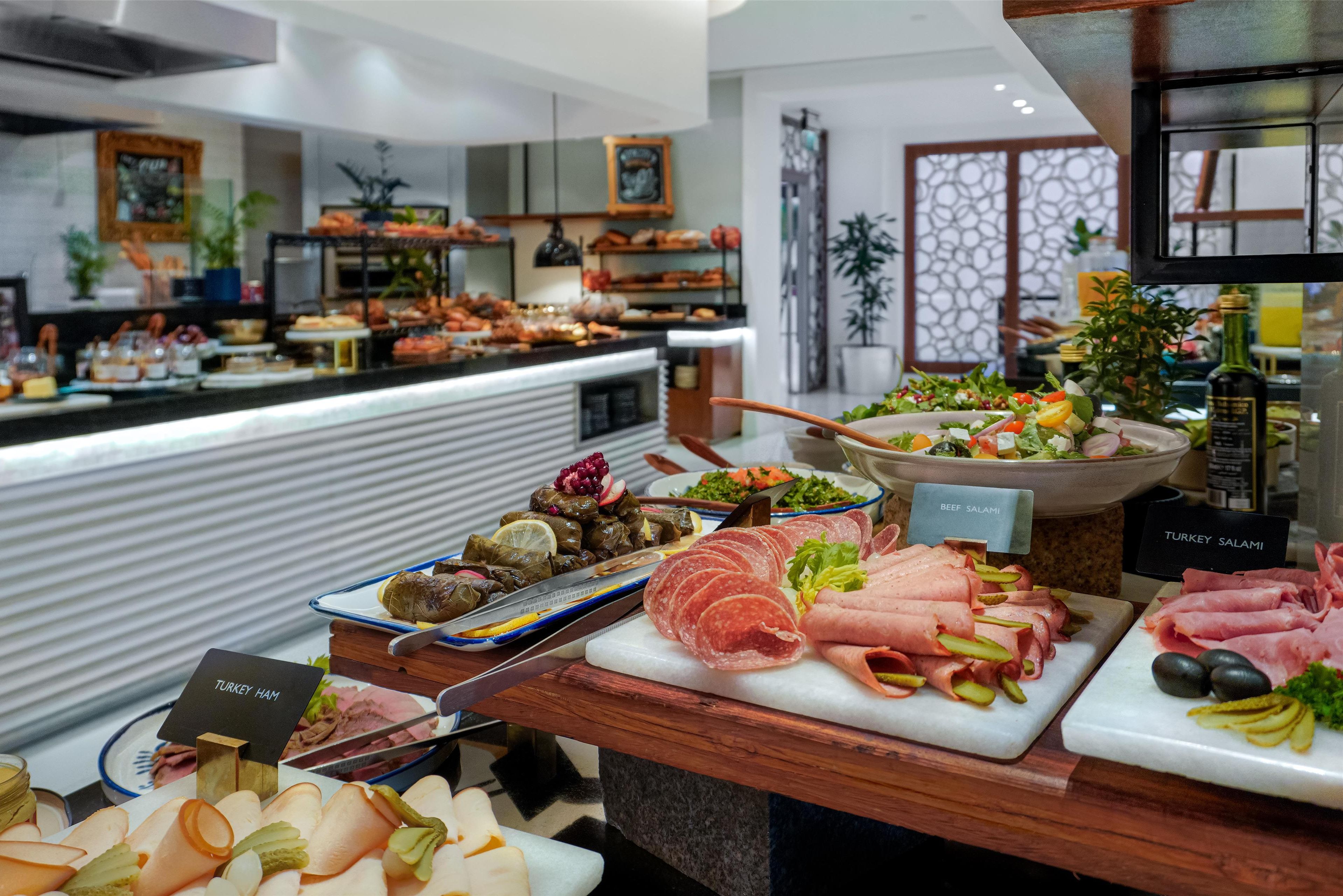 Un bufé con diversas carnes y ensaladas, incluyendo jamón de pavo, salami de res y salami de pavo.