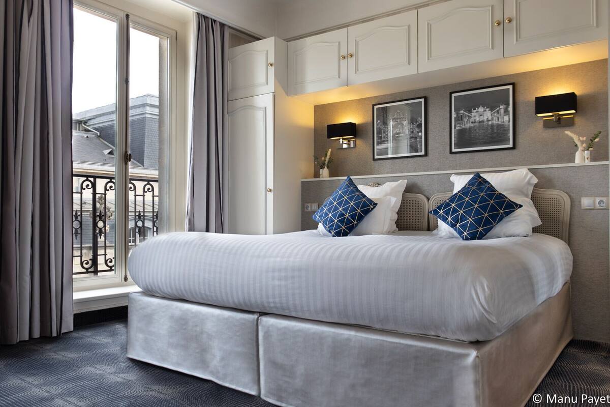 A modern hotel room with a large bed, a balcony with a view, and two wall-mounted lamps.