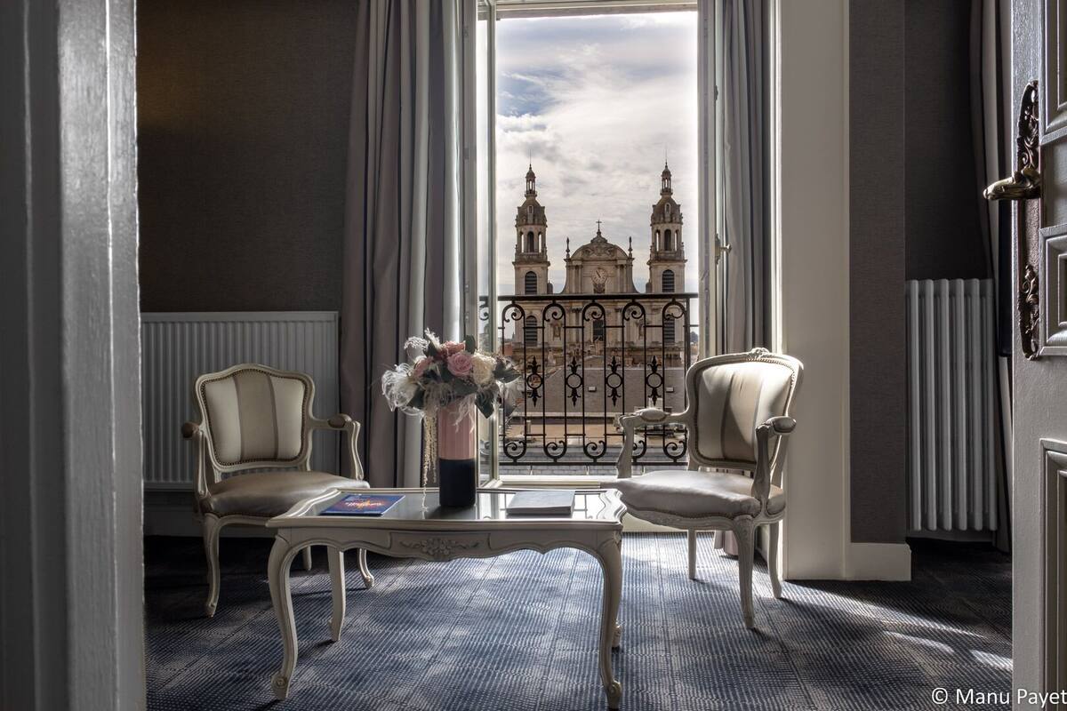 A room with two chairs, a table, and a view of a historic building through a window.