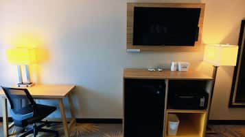 Habitación de hotel con escritorio, silla, televisión, lámparas y minibar.