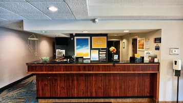 Un mostrador de recepción de hotel con detalles de madera, un reloj digital, un teléfono y un cartel que indica 'Dejar llaves aquí'.