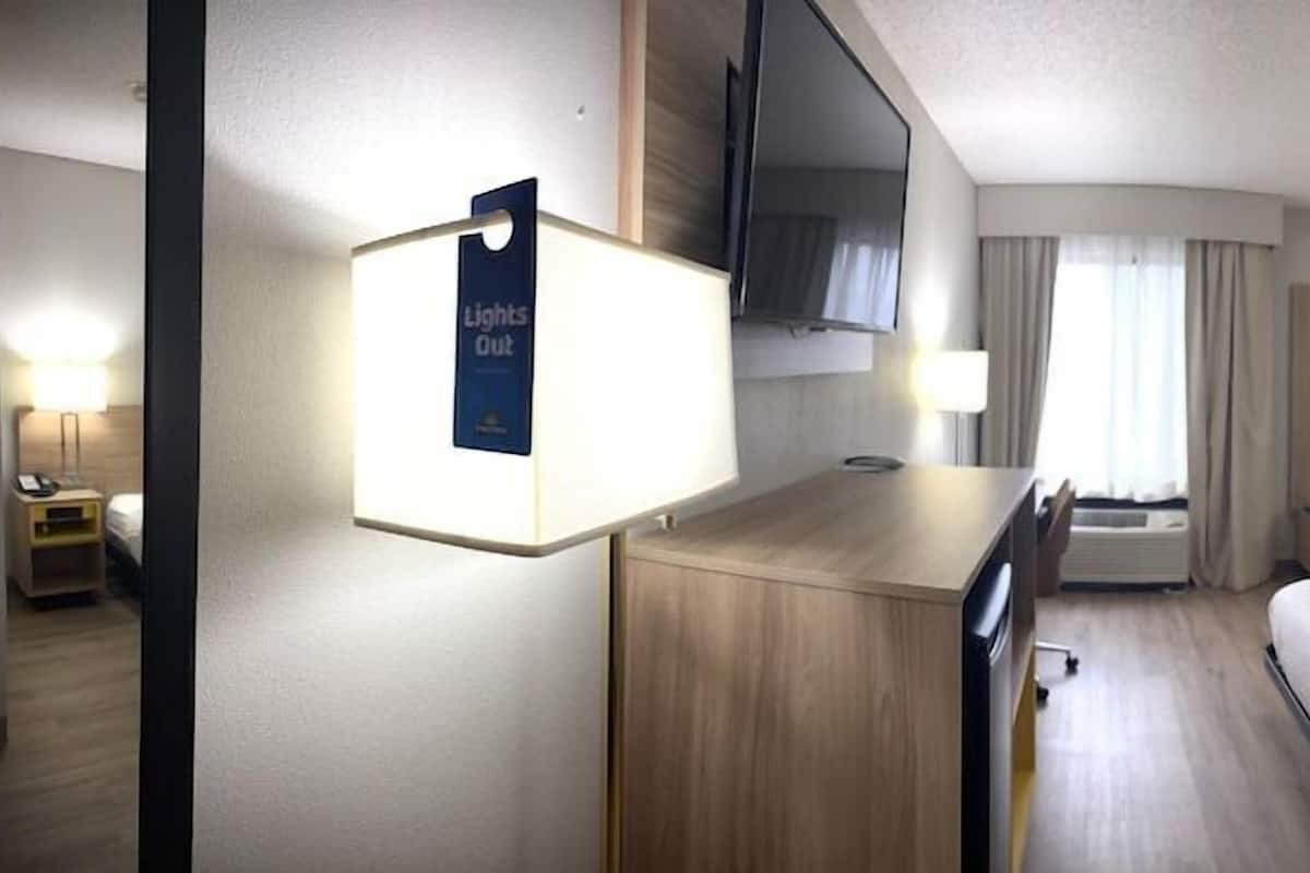 A hotel room with a bed, bedside tables, a desk, a TV, and a window with curtains.