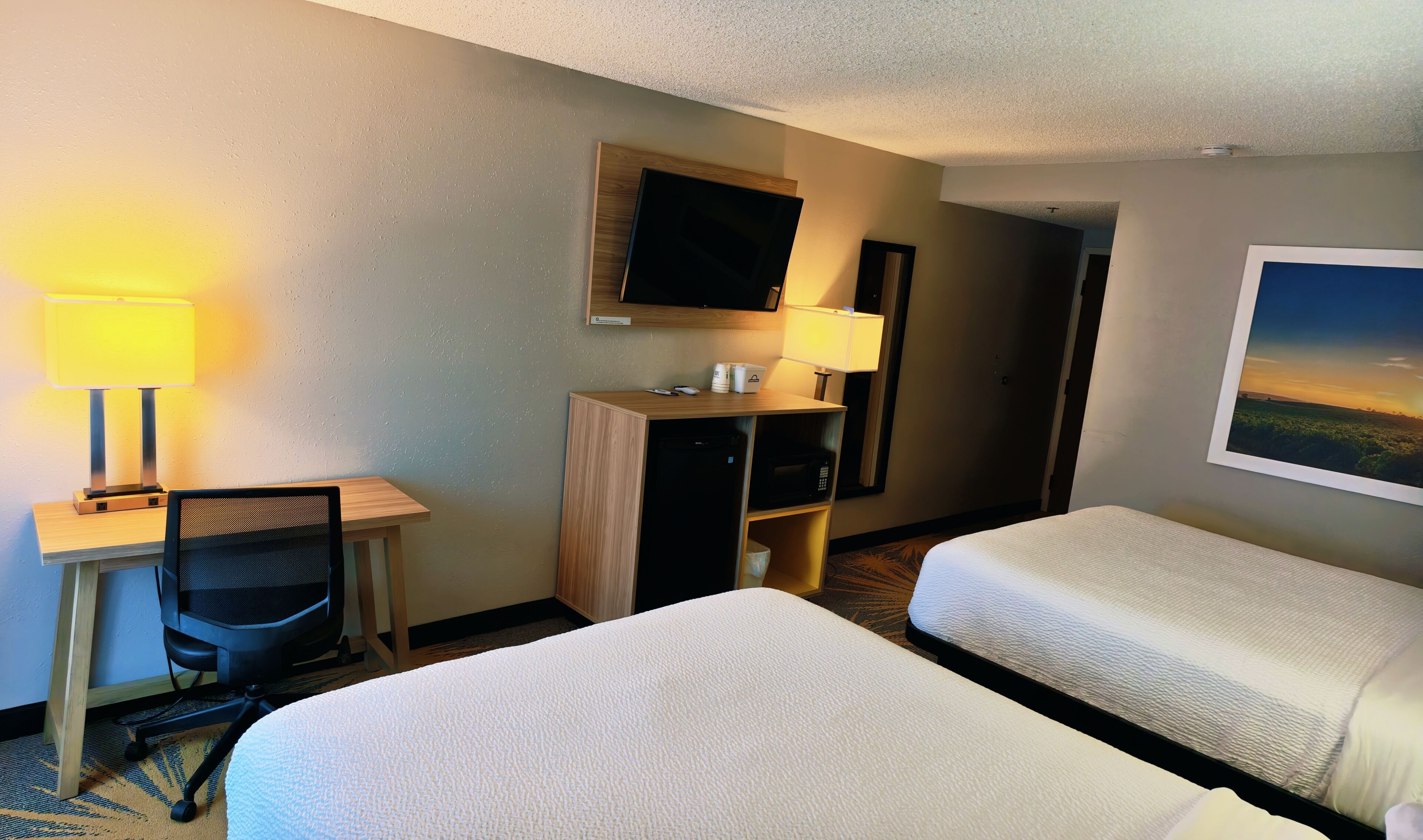 A hotel room with two beds, a desk with a chair, a television, and a picture on the wall.