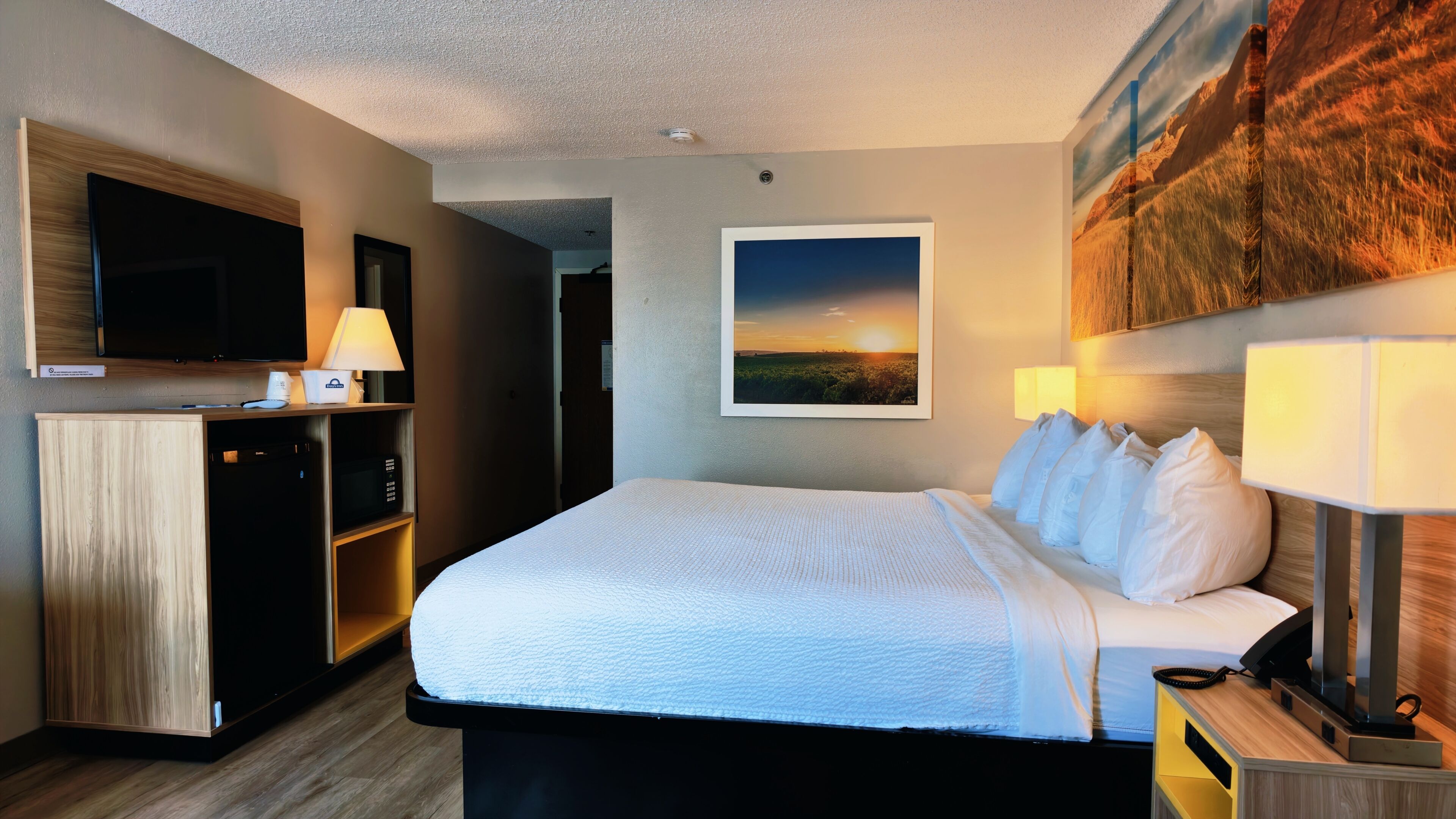 Ein Hotelzimmer mit einem Bett, einem Fernseher, einem Schreibtisch mit Lampe und einem Bild an der Wand.