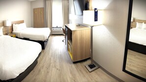 A hotel room with two beds, a desk, a mirror, a wardrobe, and a window with curtains.