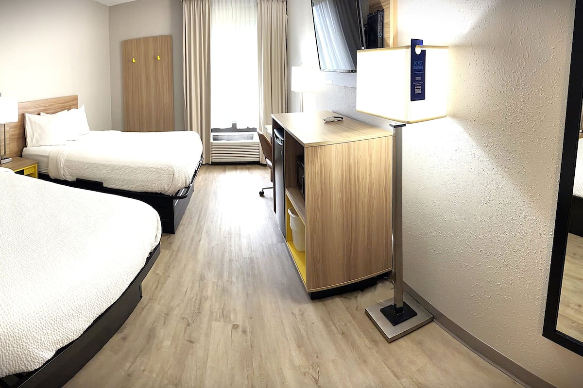 A hotel room with two beds, a desk, a mirror, a wardrobe, and a window with curtains.