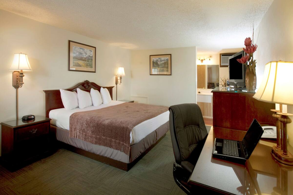 A hotel room with a bed, a desk with a laptop, a chair, a desk lamp, a nightstand, and two wall-mounted lamps.