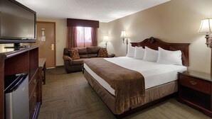 A hotel room with a large bed, a television, a sofa, and a desk with a lamp. - Best Western Torchlite (Wheatland)