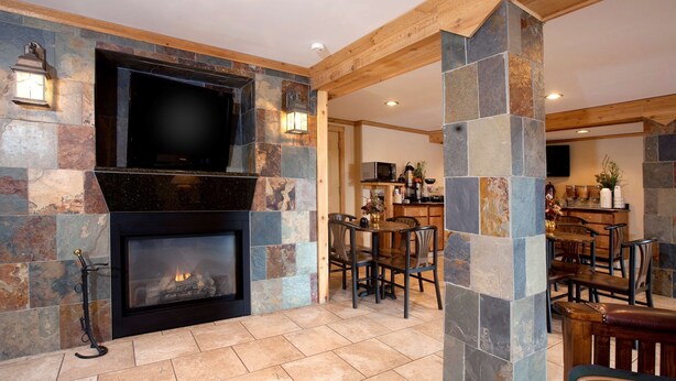 A stone fireplace with a flat-screen TV above it, surrounded by stone walls and wooden beams. - Best Western Torchlite (Wheatland)