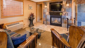 A living room with a stone fireplace, a television mounted above it, and a glass coffee table. - Best Western Torchlite (Wheatland)