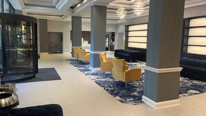 A lobby with a reception desk, seating area with yellow chairs, a dark sofa, and a patterned carpet. - DoubleTree by Hilton Baltimore North - Pikesville (Pikesville)