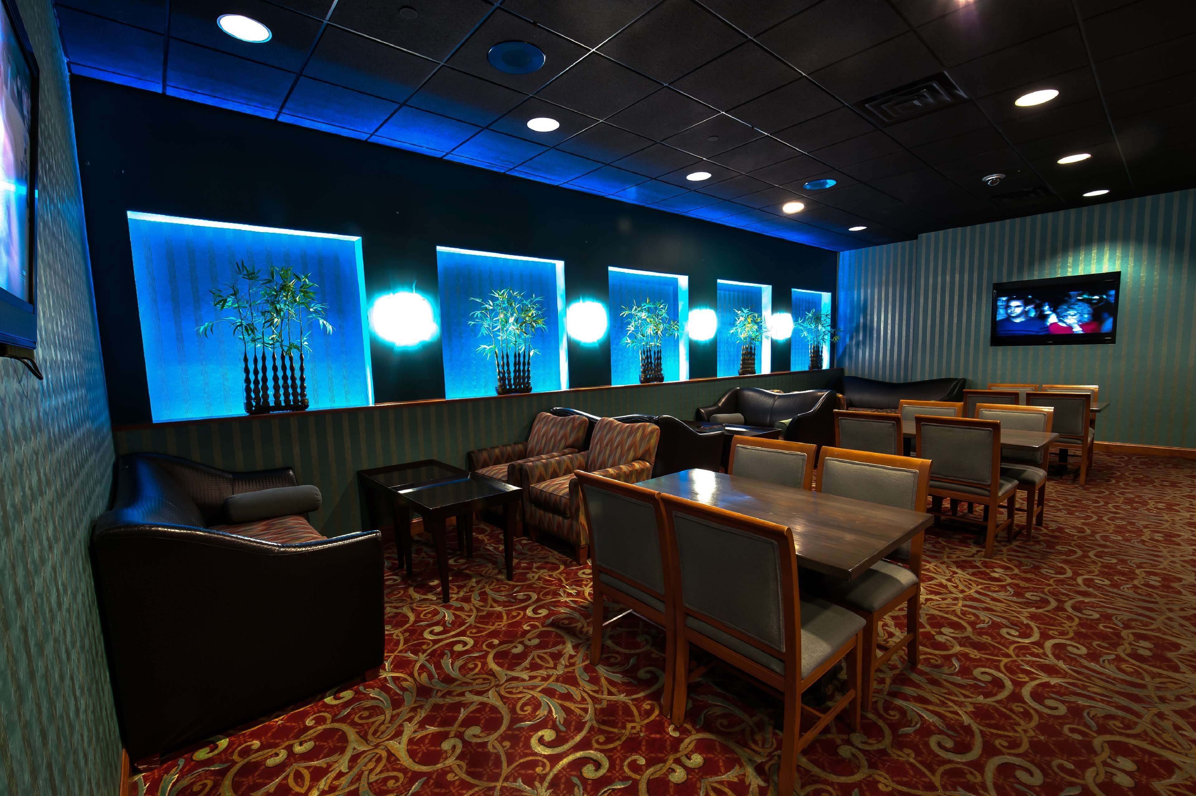A hotel lobby with a red carpet, seating area with tables and chairs, and a wall with illuminated plant displays.