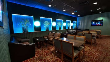 A hotel lobby with a red carpet, seating area with tables and chairs, and a wall with illuminated plant displays.
