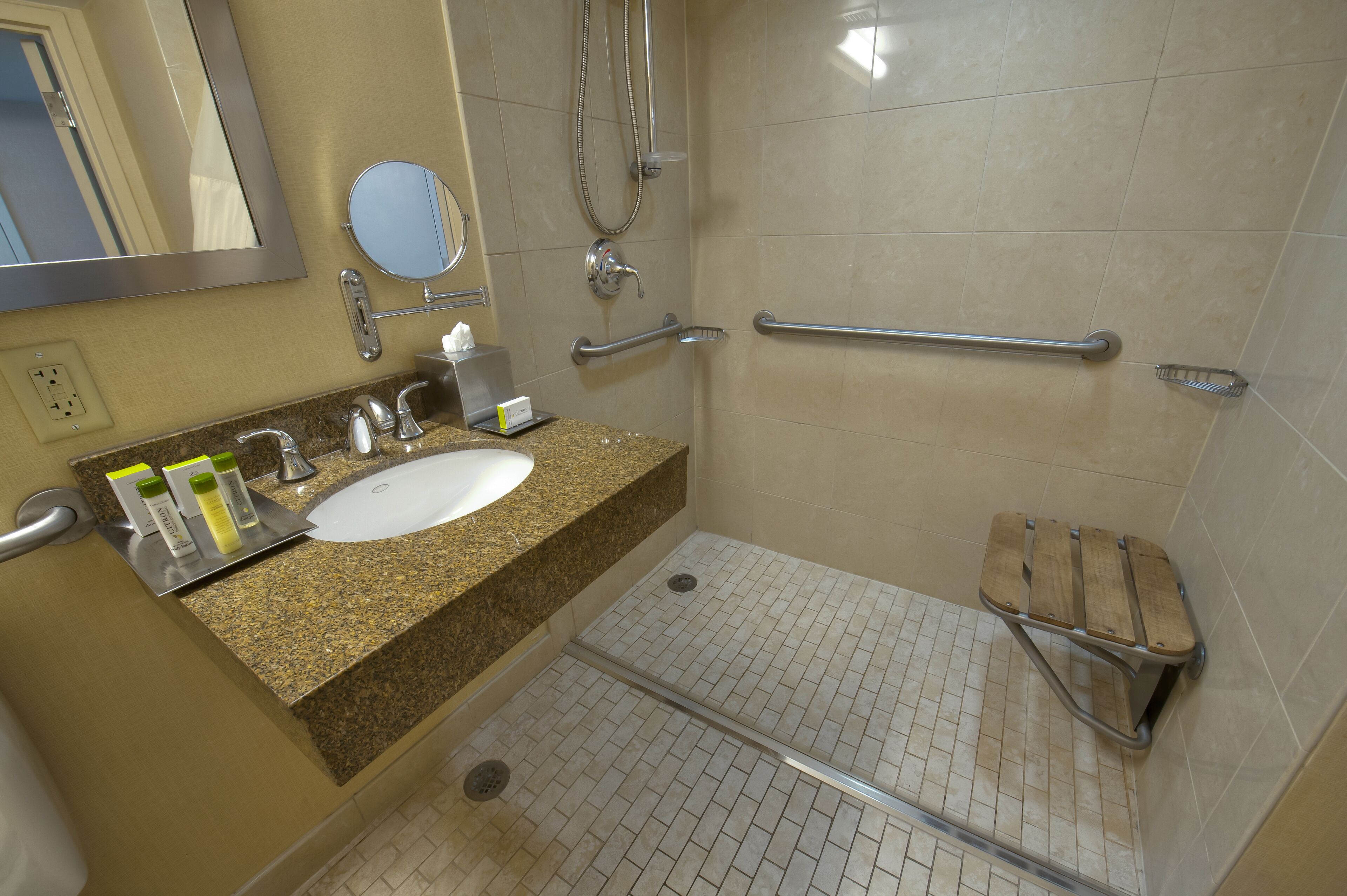 A bathroom with a sink, mirror, towel rack, shower, and grab bars.