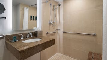 A bathroom with a granite countertop sink, a mirror, a shower with a handheld showerhead, and a grab bar.