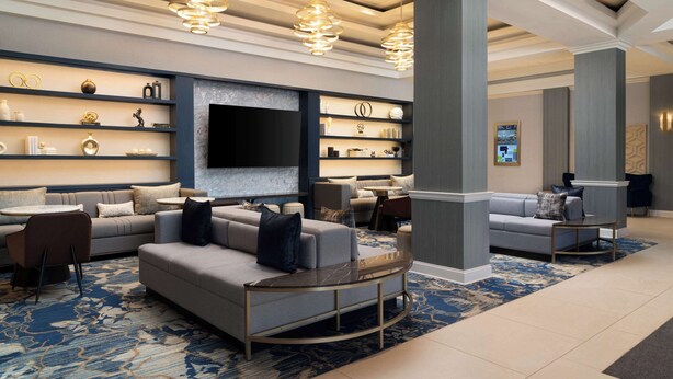 A modern hotel lobby with a large seating area, a flat-screen TV, and decorative shelves. - DoubleTree by Hilton Baltimore North - Pikesville (Pikesville)