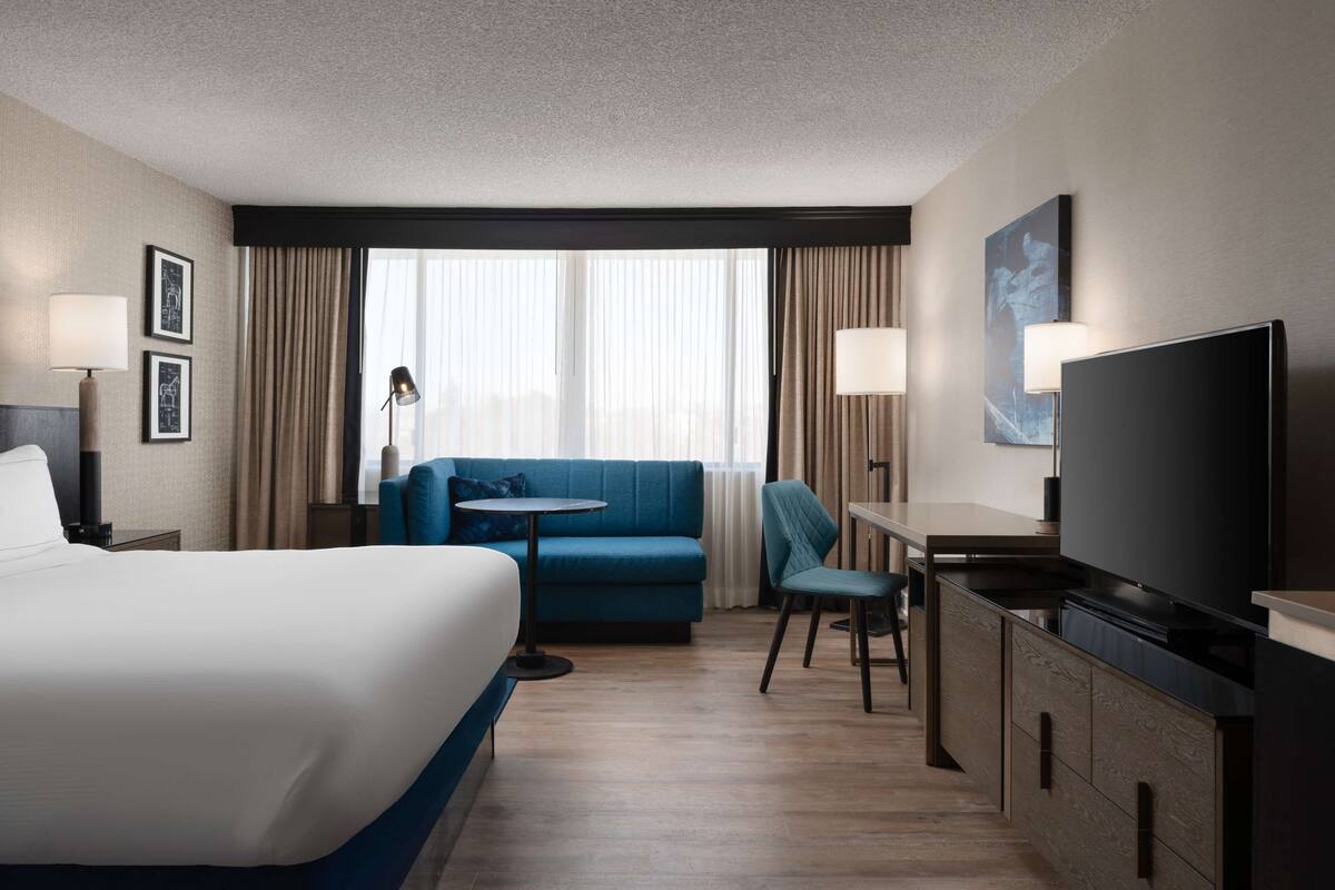 A hotel room with a large bed, a blue sofa, a small table, a TV, and a desk.