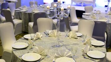 Une table ronde dressée pour un événement formel, avec de l’argenterie, de la vaisselle blanche et des verres, entourée de chaises blanches.