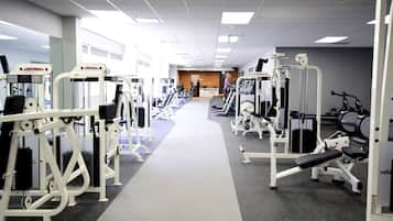 A gym with various exercise machines, a central walkway, and a reception area in the background.