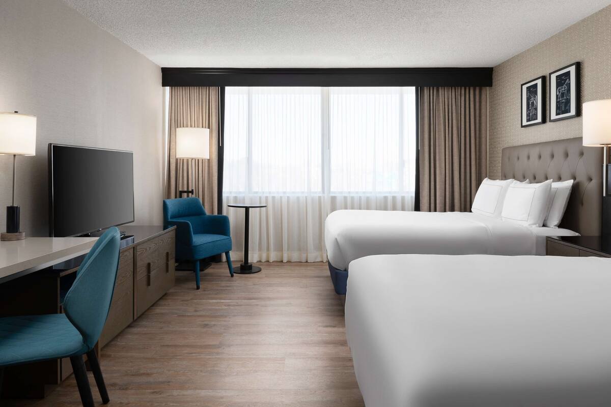 A hotel room with two beds, a desk, a chair, a TV, and a window with curtains.