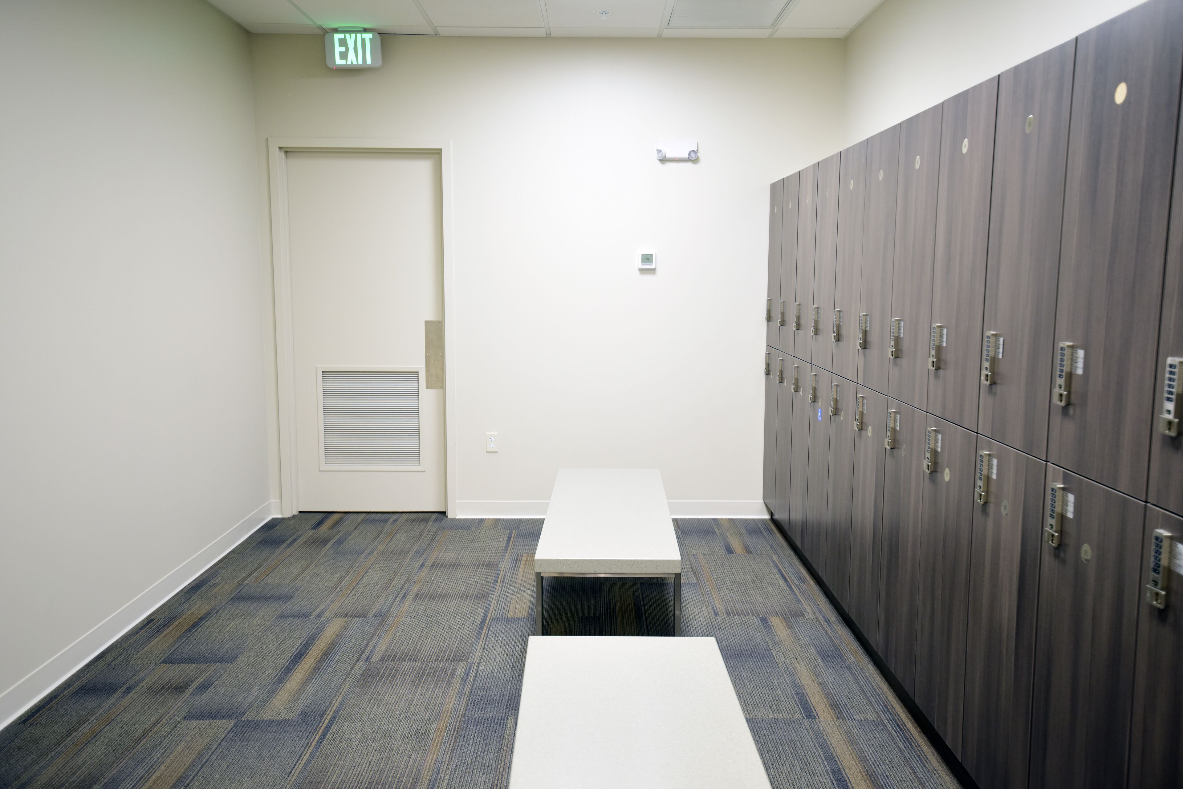 A hallway with lockers, a white door, and a bench.