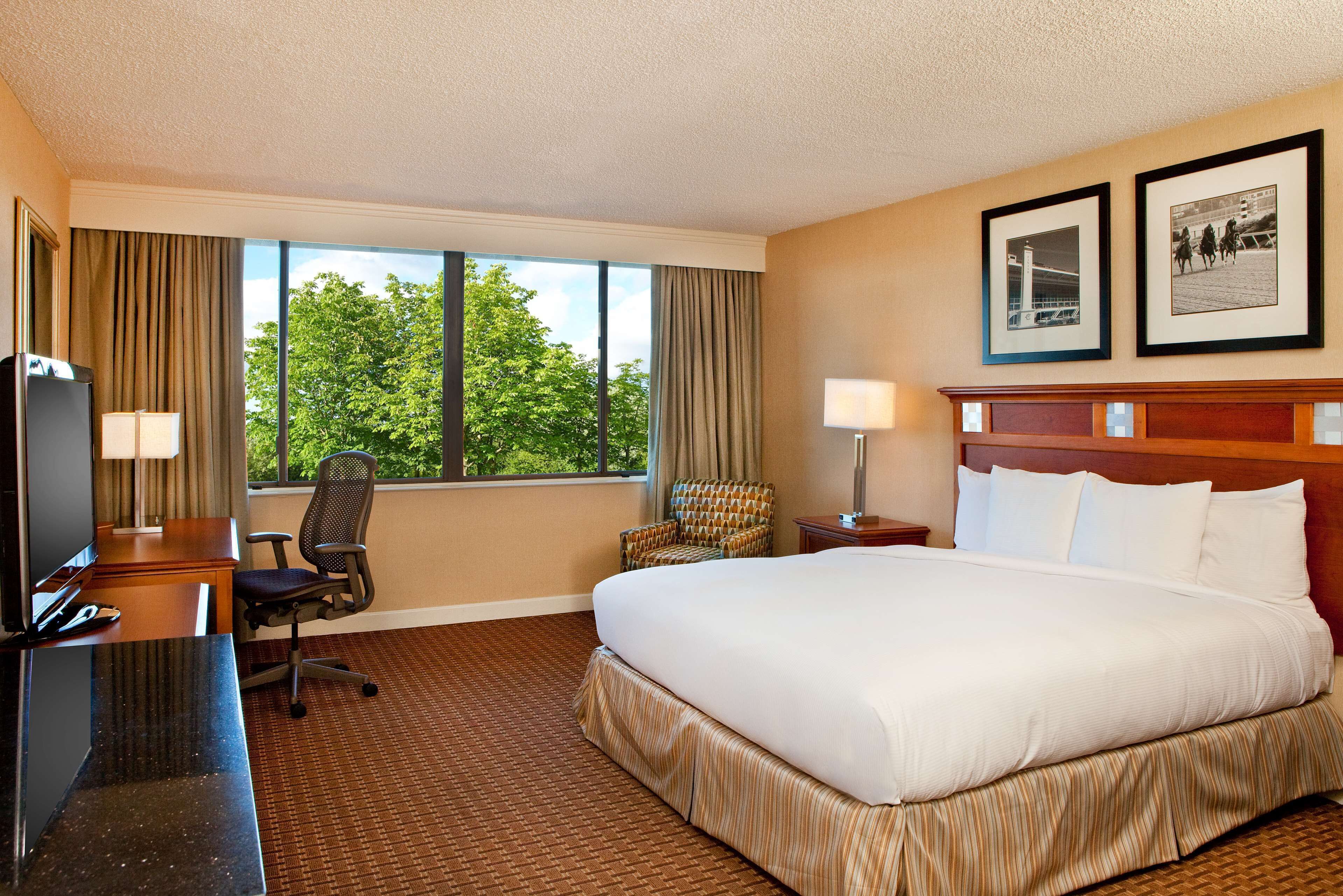 A hotel room with a large bed, a desk with a computer, a chair, a TV, and a window with curtains.