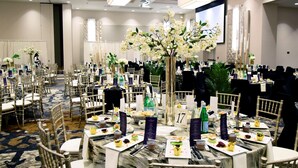 A banquet hall with round tables, chairs, floral centerpieces, and a large screen. - DoubleTree by Hilton Baltimore North - Pikesville (Pikesville)