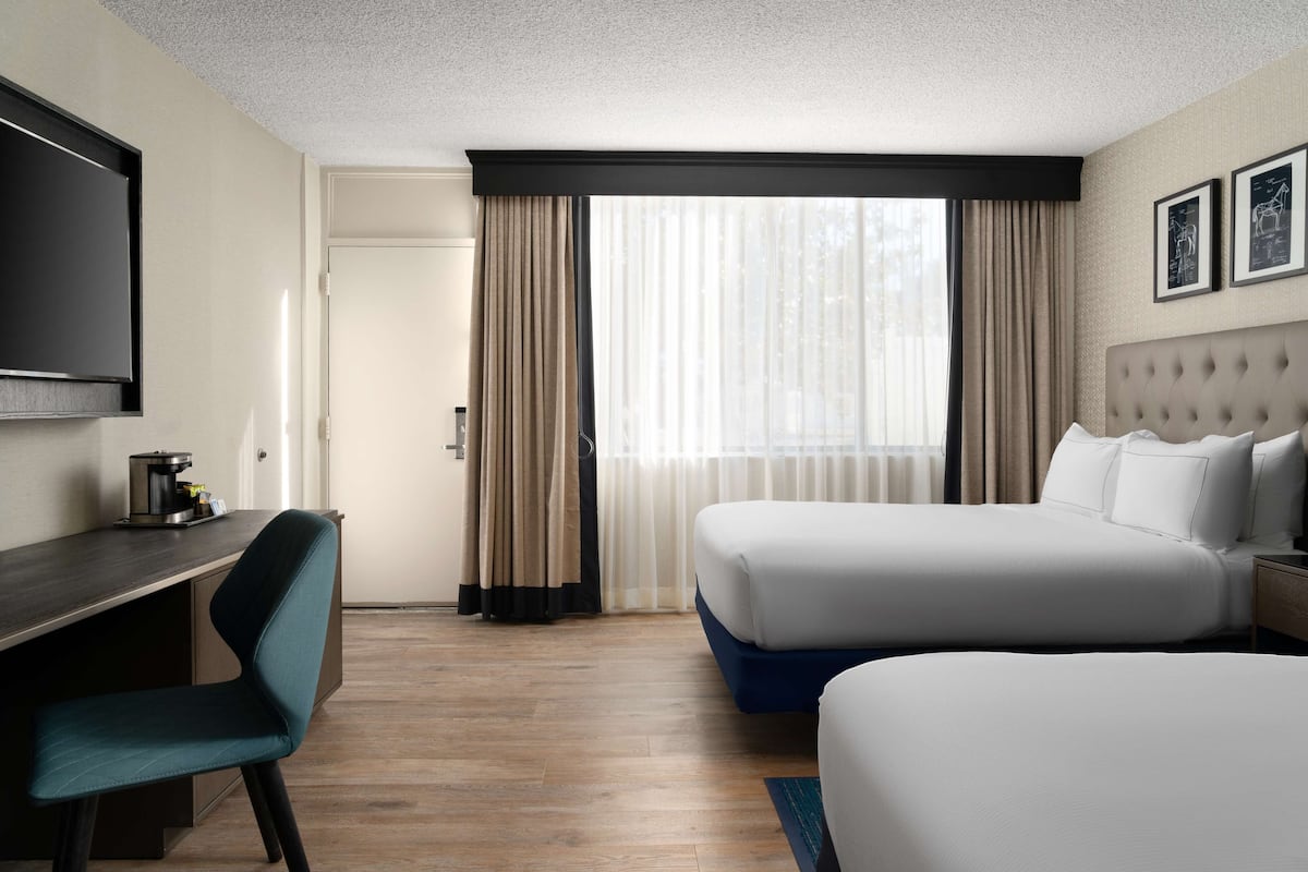 A hotel room with two beds, a desk, a chair, a TV, and a window with curtains.