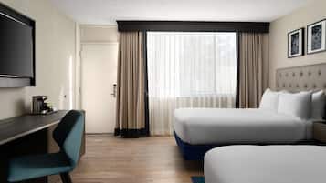 Quarto de hotel com duas camas, uma escrivaninha, uma cadeira, uma televisão e uma janela com cortinas.