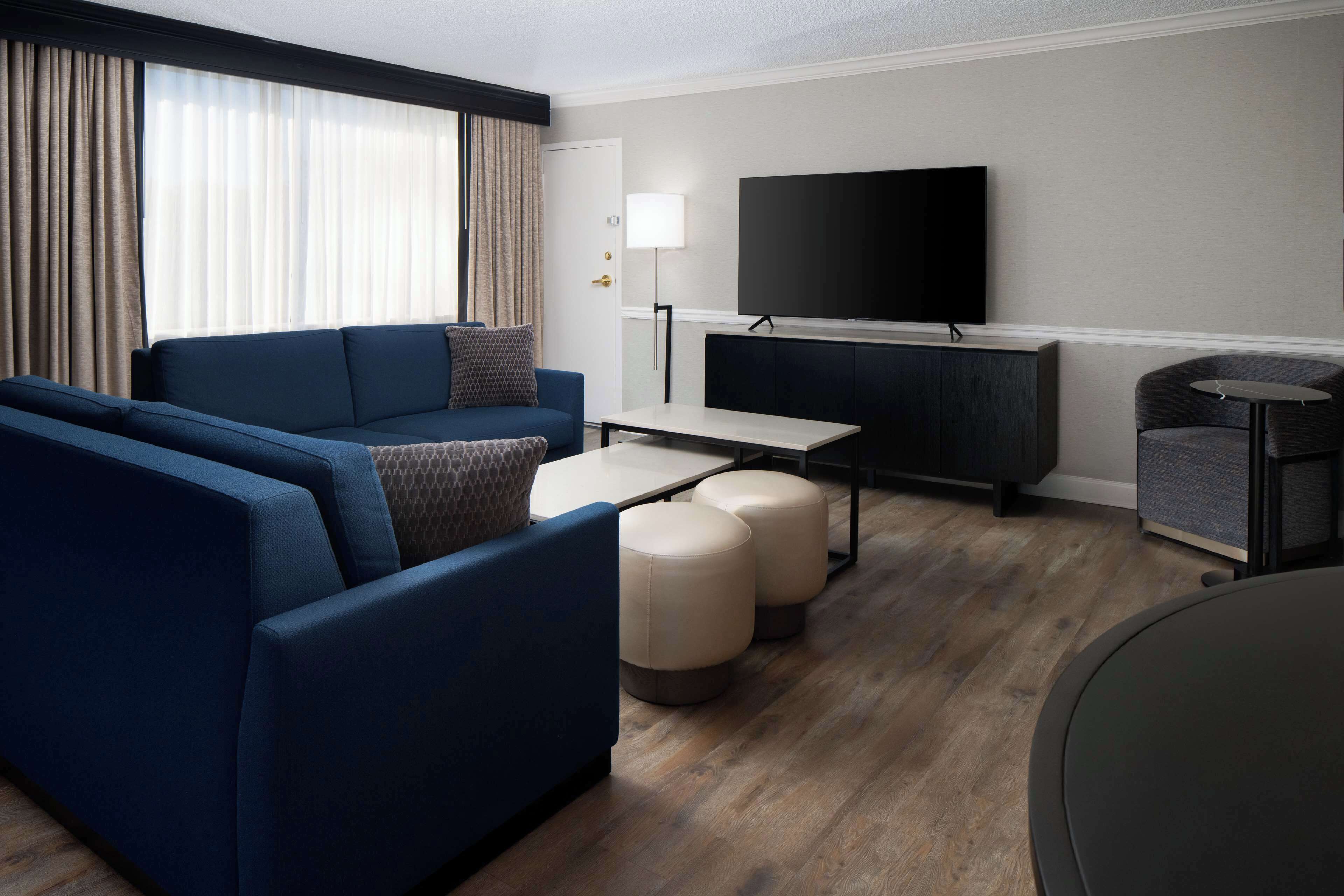 A modern living room with a blue sofa, ottomans, a small table, and a flat-screen TV mounted on the wall.