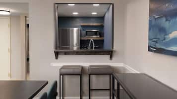 Una cocina compacta con refrigerador, microondas y lavamanos, un comedor con mesa y sillas, y un cuadro en la pared.