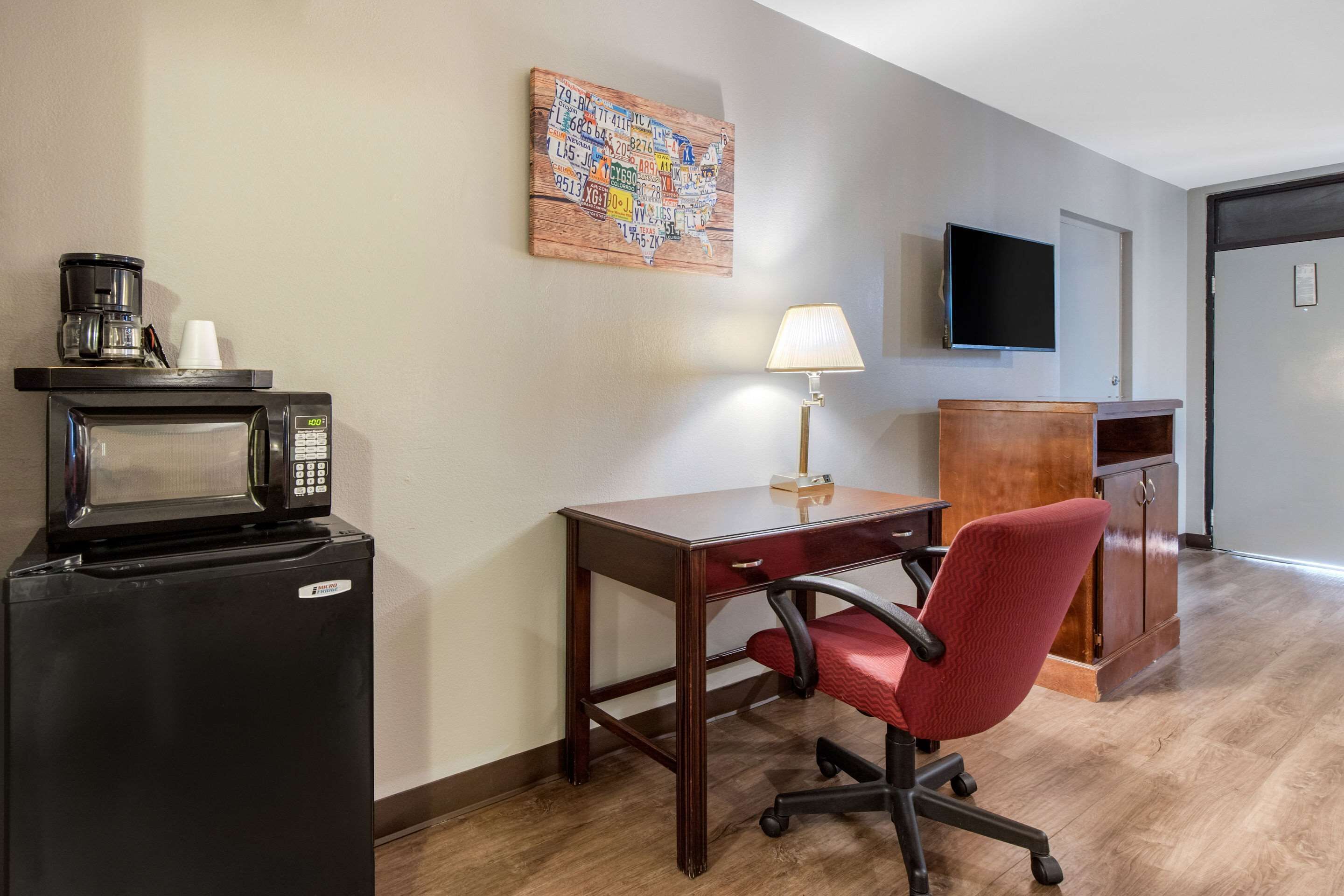 A hotel room with a kitchenette, a desk, a red office chair, a wooden cabinet, a television, and a wall map.