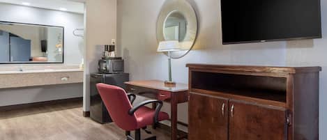 Habitación de hotel con un escritorio de madera, una silla de oficina roja, un televisor de pantalla plana, un espejo y una cafetera.