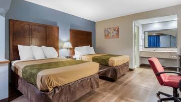 A hotel room with two beds, a desk, a chair, and a bathroom visible through an open door.