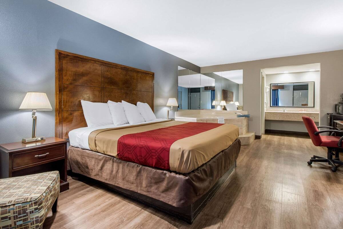 A hotel room with a large bed, a nightstand, a chair, a desk, and a mirror.