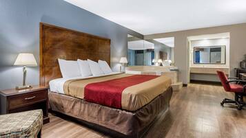 A hotel room with a large bed, a nightstand, a chair, a desk, and a mirror.