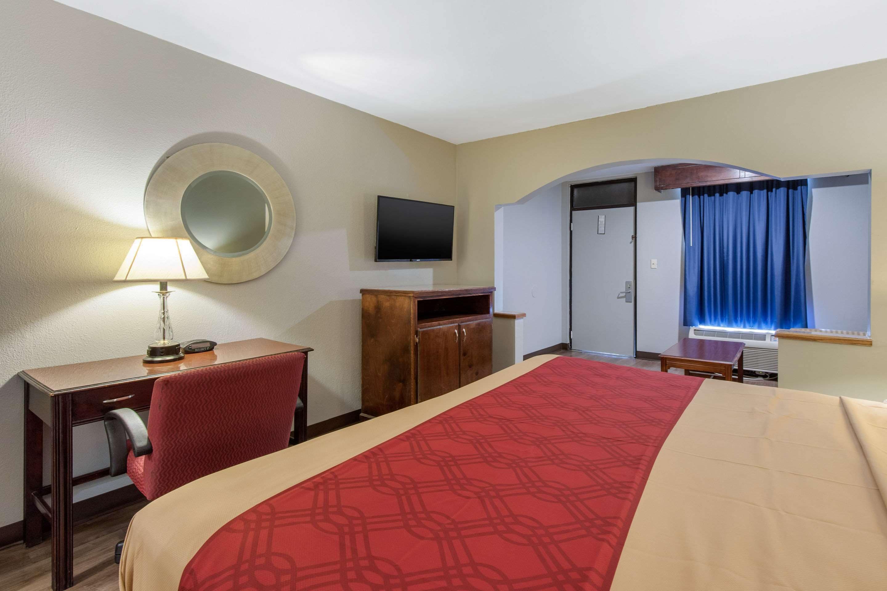 A hotel room with a bed, desk, chair, TV, and a mirror on the wall.