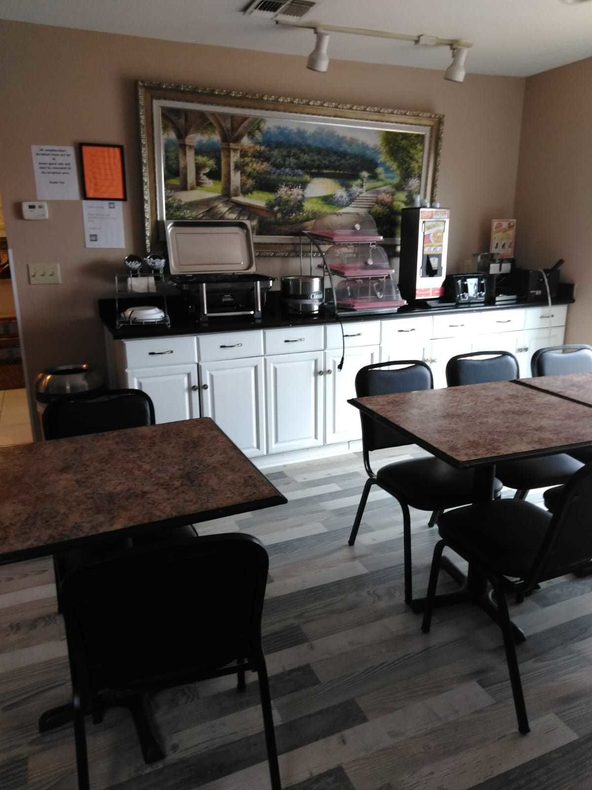 A small dining area with a table and chairs, a kitchen area with appliances, and a framed painting on the wall.