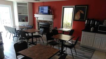 A restaurant with tables and chairs, a fireplace, a television, and a window with a view.
