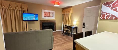 Habitación de hotel con sofá, mesa de comedor, chimenea, televisor y puerta.